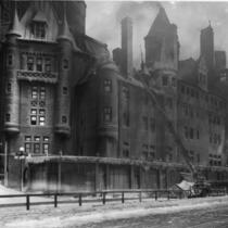 De la fumée s’échappe du Château Frontenac. Des pompiers se trouvent devant l’édifice, ainsi qu’une calèche et deux chevaux. 