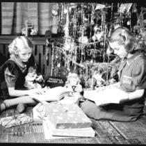 Deux fillettes jouent avec leurs cadeaux au pied d’un arbre de Noël.
