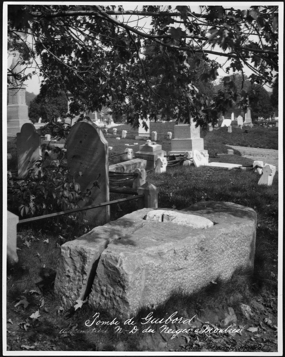 Une pierre couchée à l'horizontal sans croix est entourée de pierres tombales 