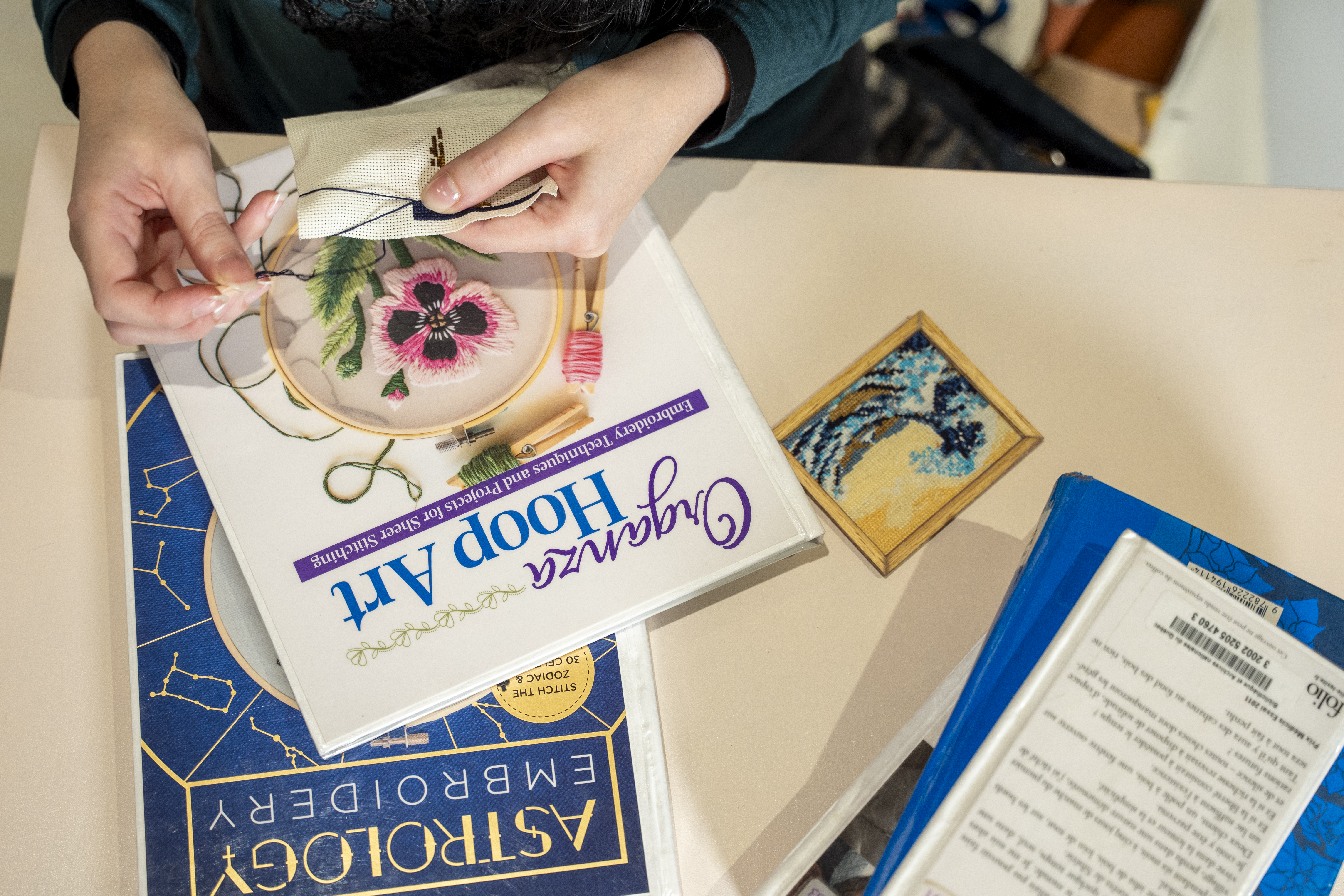 Les femmes d'une femme faisant de la broderie au-dessus des livres Organza Hoop Art et Astrology Embroidery, posés sur une table.