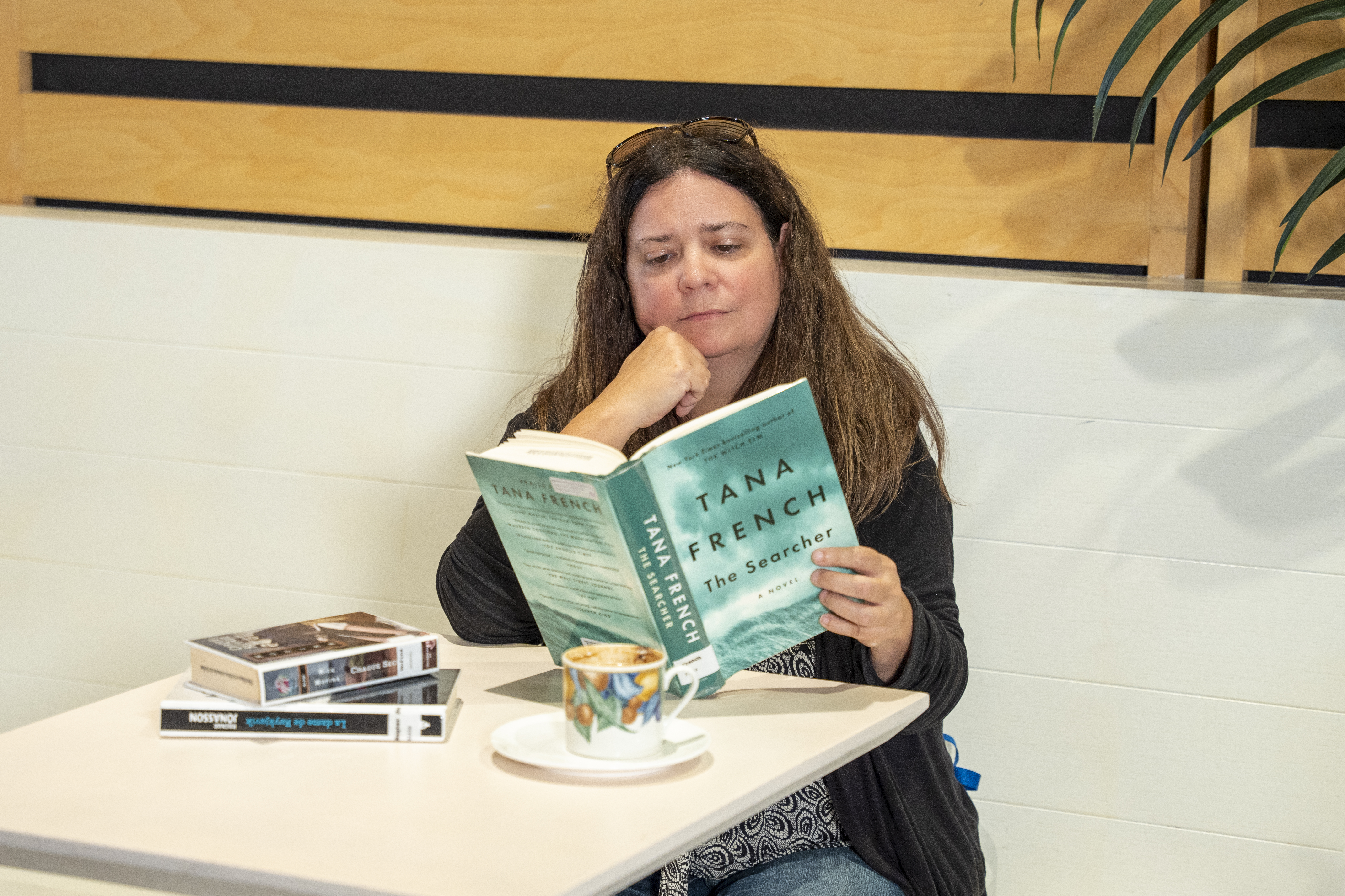 Une femme attablée devant un café lit La colline aux disparus, de Tana French.