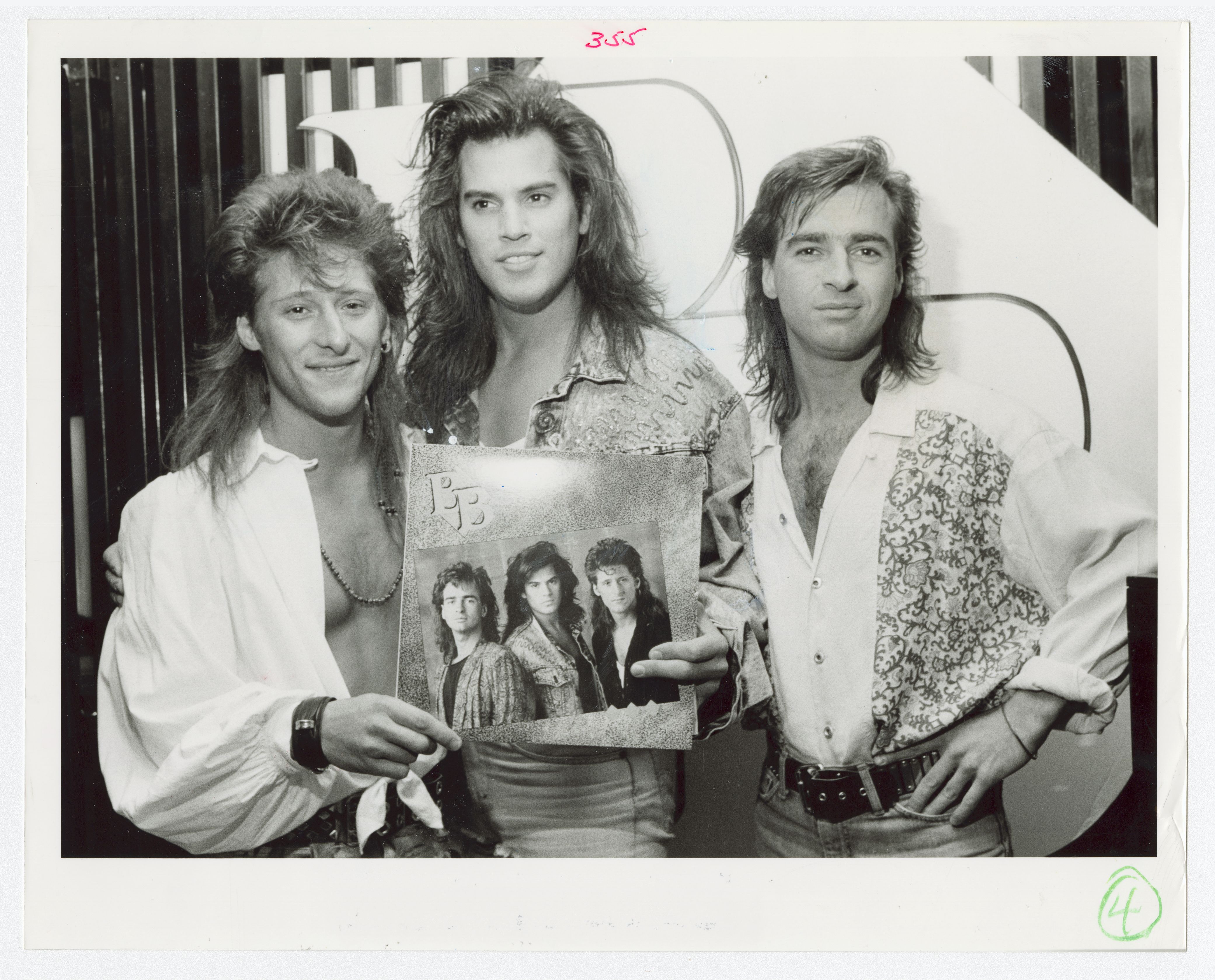 Les trois hommes formant le groupe les B.B. posent pour la caméra. Ils tiennent dans leur main l’album du groupe en format vinyle.