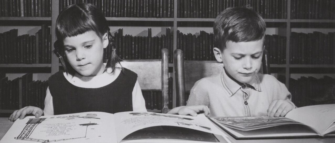 Un garçon et une fille lisent respectivement un livre, assis à une table à la bibliothèque.