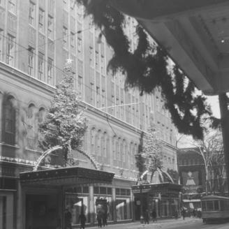 Nous voyons la façade du magasin à rayons Eaton's de la rue Sainte-Catherine Ouest à Montréal. Il y a un arbre de Noël sur les deux marquises des portes d'entrée.