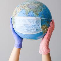 deux mains avec des gants en latex tenant un globe terestre portant un masque médical bleu 